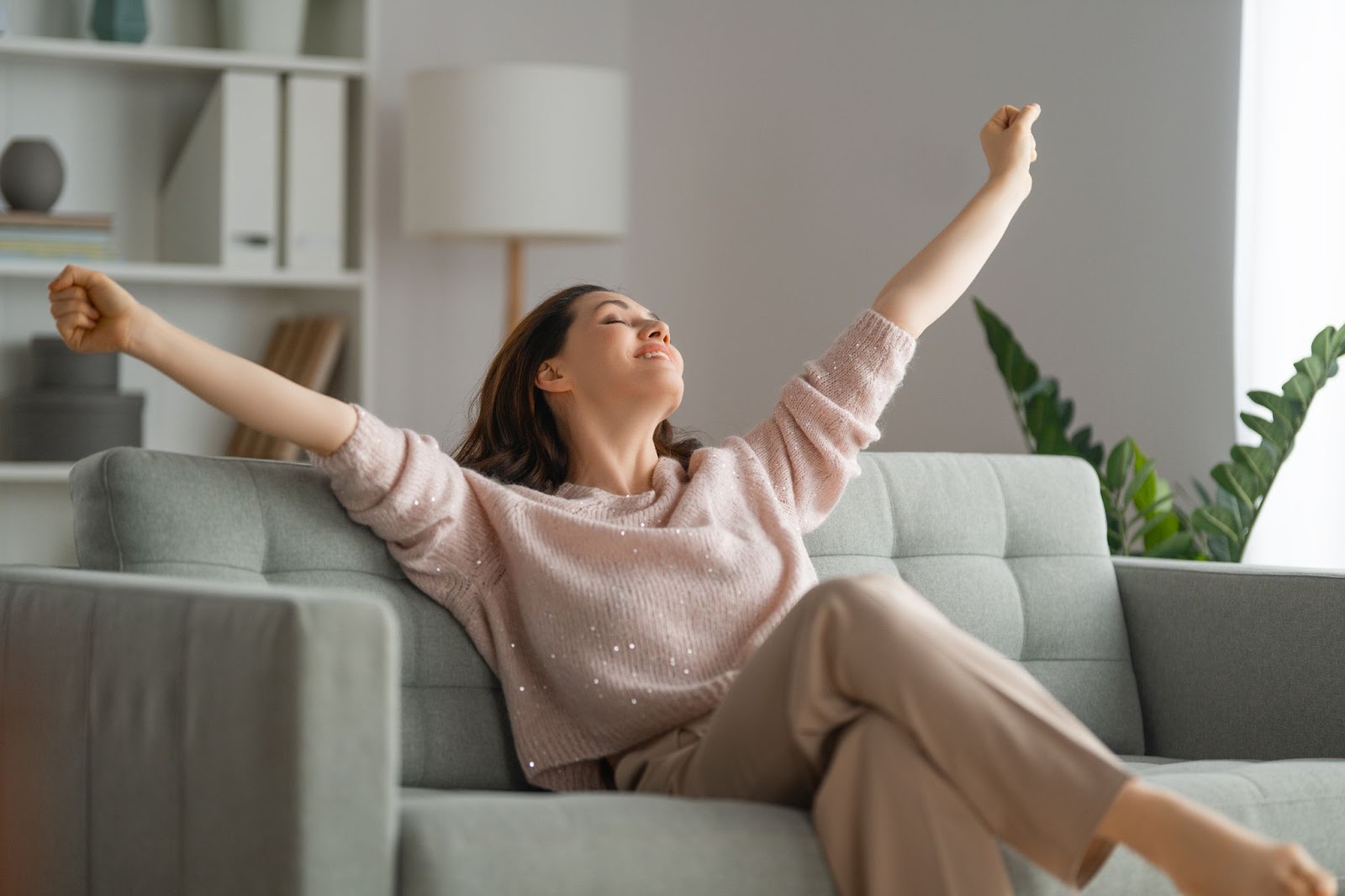 A woman on a couch with arms raised, symbolizing relaxation after completing a professional cleaning checklist.