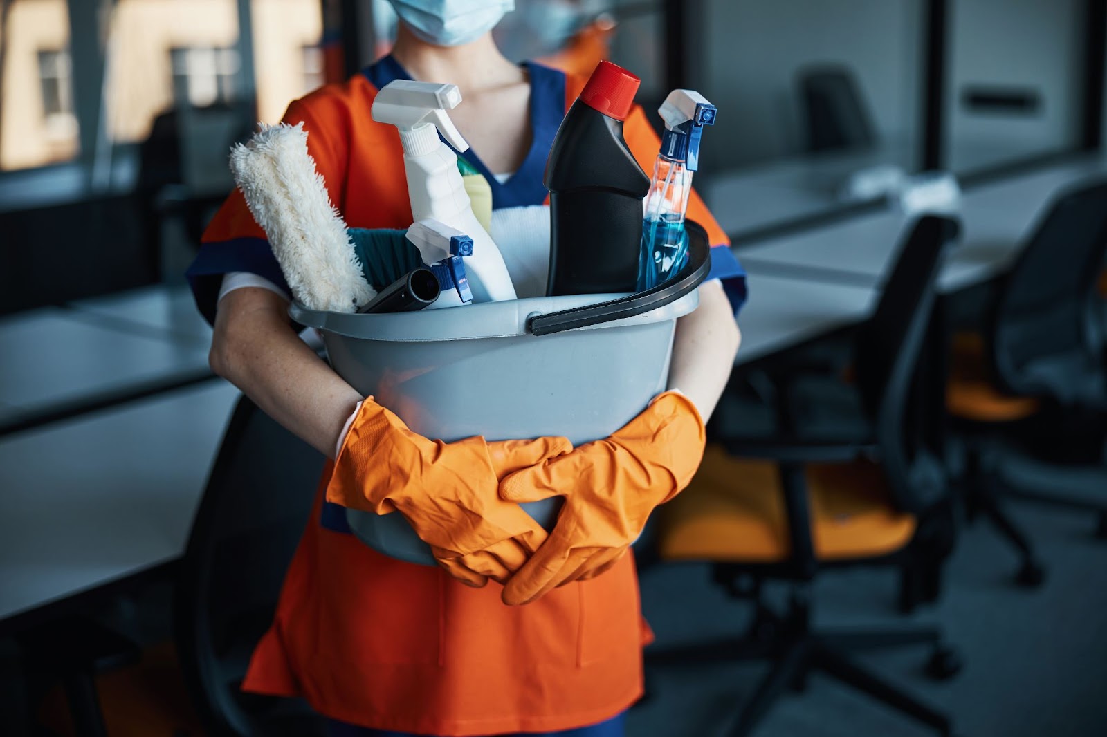 A woman in an orange uniform holds a bucket of cleaning supplies, symbolizing professional cleaning and the gift of cleanliness.